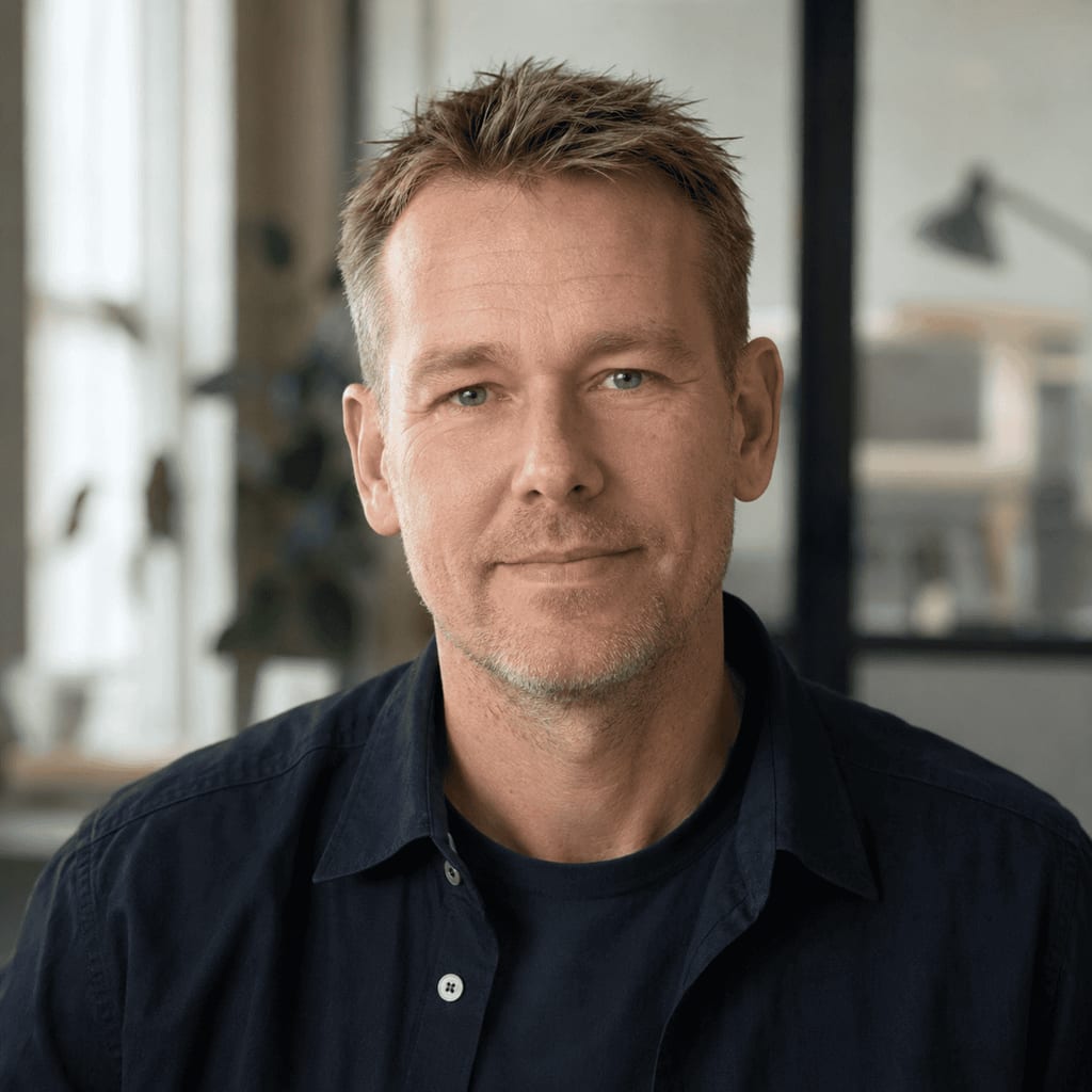 Portrait of a man with short hair wearing a dark shirt, smiling in an office setting.